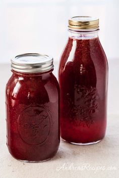 two jars filled with red liquid sitting on top of a white tablecloth next to each other