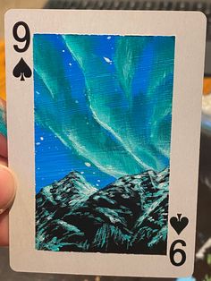 a hand holding up a playing card with an image of the sky and mountains on it