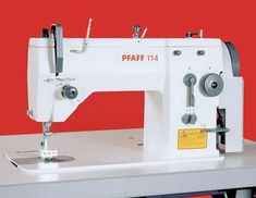 a white sewing machine sitting on top of a metal table next to a red wall