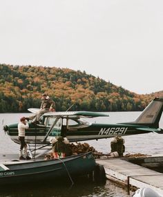 a small plane sitting on top of a body of water next to a boat with people boarding it