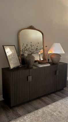 a large mirror sitting on top of a wooden cabinet next to a lamp and vase