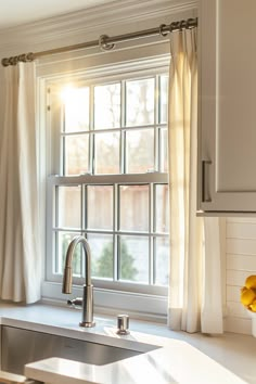 a kitchen sink sitting under a window next to a metal faucet and counter top