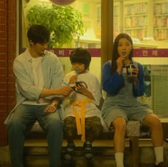 three people sitting on a bench in front of a window while one person uses his cell phone