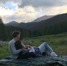 a man and woman are sitting on a blanket in the mountains