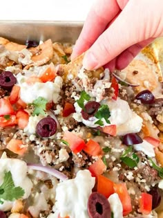 a hand picking up a piece of bread with olives and feta cheese on it