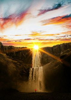 a person standing in front of a waterfall at sunset