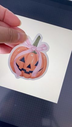 a hand holding an orange pumpkin shaped sticker