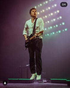 a man standing on top of a stage with a guitar in his hand and lights behind him