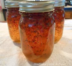 three jars filled with food sitting on top of a white tablecloth covered countertop