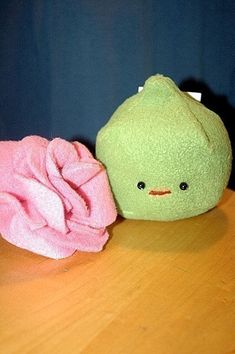 a green stuffed animal next to a pink towel on a wooden table with blue walls