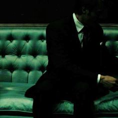 a man sitting on top of a green couch next to a black wall in a dark room