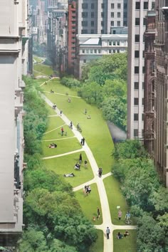 an aerial view of people walking and sitting on the grass in a park with tall buildings