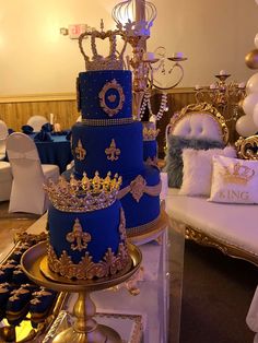 a three tiered blue cake with gold trimmings sits on a table in front of balloons