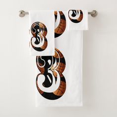 two towels hanging on a towel rack in front of a white wall with black and orange designs