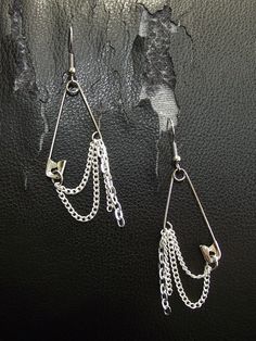 two pairs of earrings with chains hanging from them on a black leather surface, one is silver and the other is white