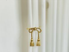 two golden tassels hanging from the side of a curtain in front of white drapes