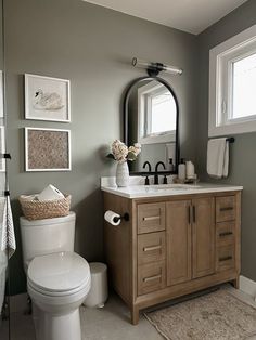 a white toilet sitting next to a bathroom sink under a mirror and framed pictures on the wall