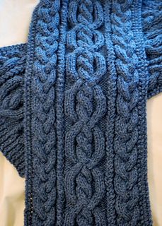 a blue knitted sweater is hanging on a white surface with the top part folded up