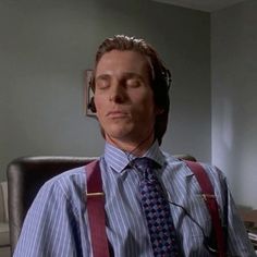 a man wearing suspenders and a tie sitting in an office chair with his eyes closed