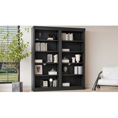 a black bookcase with many books on it in front of a white couch and window