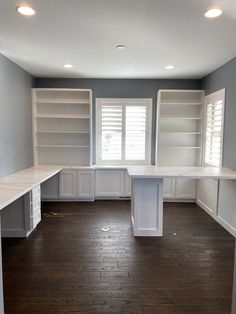 an empty room with white cabinets and wood flooring in the center, along with two windows that have shutters on both sides