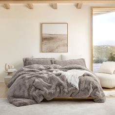 a bedroom with a large bed covered in grey blankets and pillows, next to a white couch