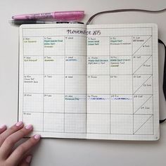 a hand holding a pen over a notebook with calendars on it and a pink marker next to it