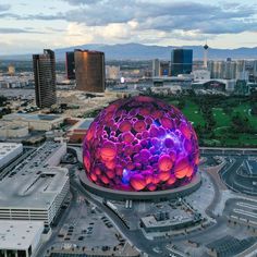 an aerial view of a large building with purple lights on it's roof and buildings in the background