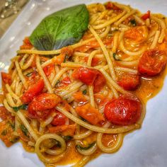 pasta with tomatoes and spinach on a white plate, garnished with basil