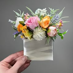 a person is holding a flower arrangement in their hand