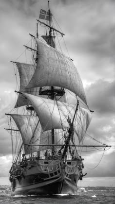 a black and white photo of a large sailboat in the ocean under cloudy skies