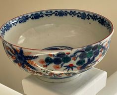 a bowl is sitting on top of a white pedestal with flowers and leaves painted on it