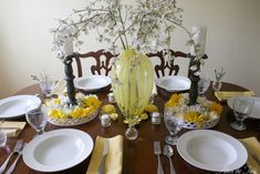 a dining room table set with white plates and yellow napkins, silverware and flowers