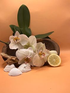 an arrangement of orchids, lemon and seashells in a wooden bowl on orange background