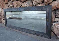 a large mirror sitting on the side of a road next to a stone wall,