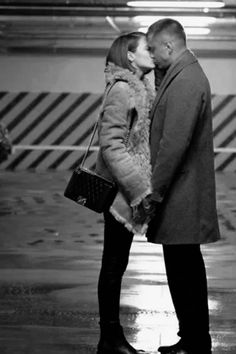 a man and woman kissing in front of an airplane at the airport on a rainy day