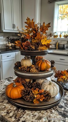 three tiered trays filled with pumpkins and pine cones