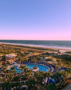 an aerial view of the beach and pool area at sunset or sunrise, with palm trees in foreground