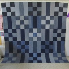 a blue and gray checkered quilt hanging on a wall next to a vase with purple flowers