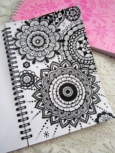 two notebooks with black and white designs on them sitting on a lace tablecloth