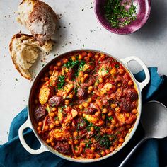 a pot filled with chickpeas and bread on top of a blue cloth next to two bowls