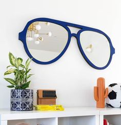 a white shelf topped with a mirror next to a potted plant and a cactus