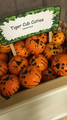 oranges with faces drawn on them are in a cardboard box and have signs that say tiger cub cuts