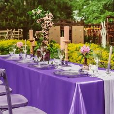 a long table with purple linens is set up for an outdoor dinner in the garden