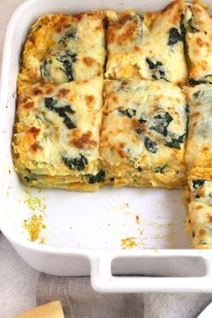 a casserole dish with cheese and spinach on top, cut into squares