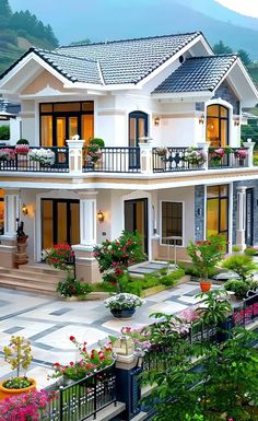 a large white house with lots of windows and flowers in the front yard, surrounded by greenery