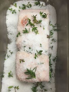 two pieces of fish covered in sea salt and herbs on top of some white snow