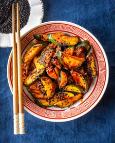 a bowl filled with food next to chopsticks on top of a blue table cloth