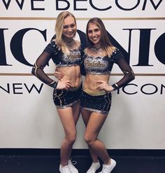 two beautiful young women standing next to each other in front of a wall with words on it