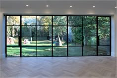 an empty room with large windows and wood flooring on one side, trees in the background